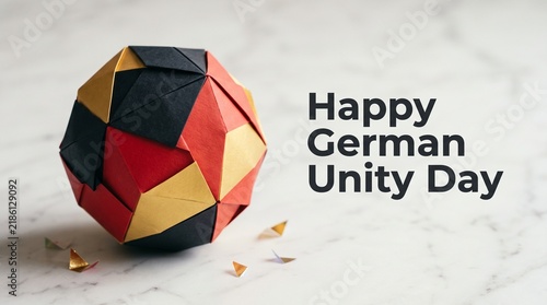 German Unity Day greeting with origami paper ball, national flag colors on marble background, patriotic holiday celebration
