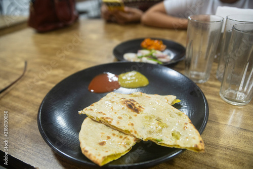 Indian Stuffed Flatbread Aloo paratha with Chutneys on a Black Plate