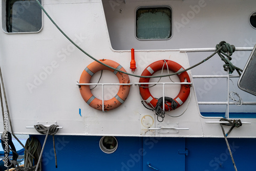 Cuadro en lienzo Two orange life preservers are attached to the white hull of a boat, with ropes