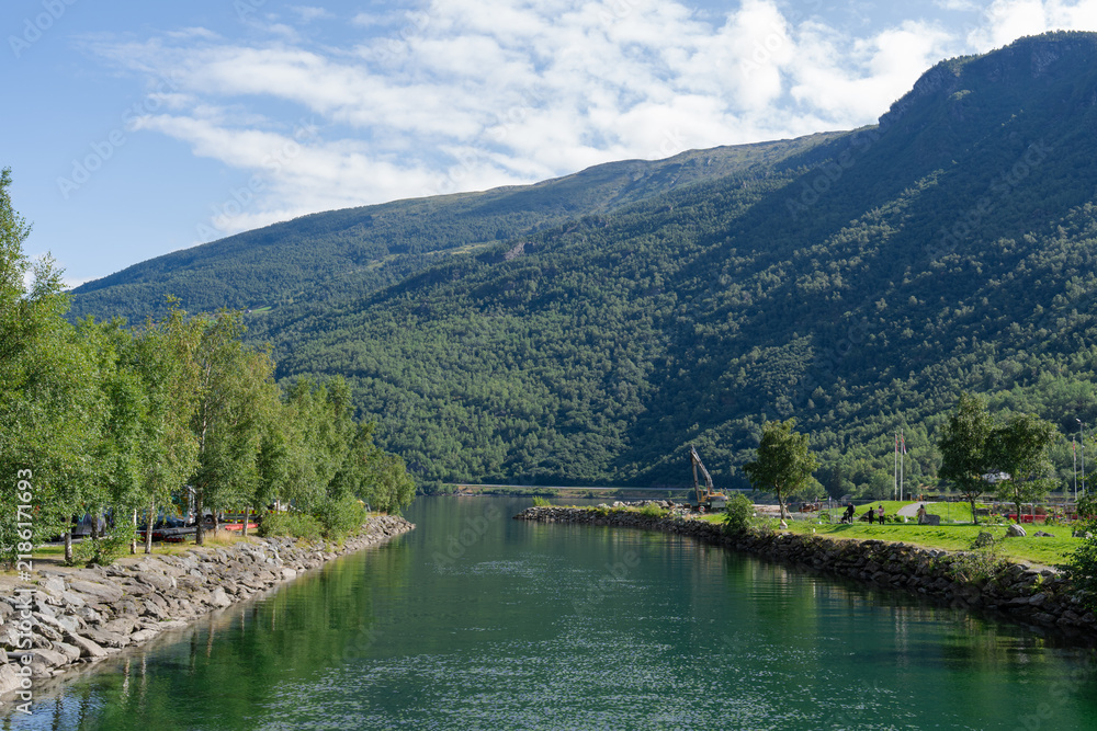 Obraz premium Scenic river view with green trees, rocky banks, and majestic mountains