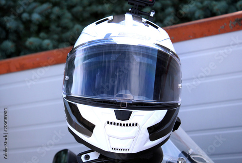 White and black motorcycle helmet with a clear visor, angular shell, glossy panels, ventilation ports, and dark trim, photographed in close-up against a blurred outdoor background.