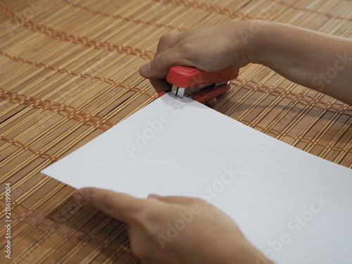 Принти на полотні Holding a stapler in right hand and the paper in left, small pink stapler is used to staple corner of sheet of white paper resting on a woven bamboo surface
