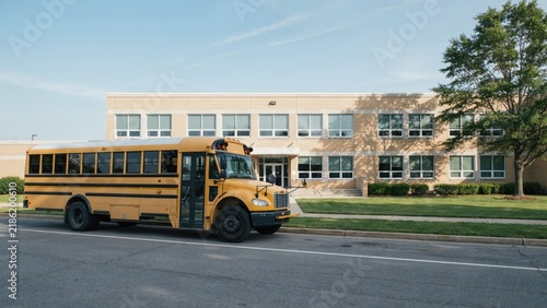 Yellow School Bus Parked in Front of a Brick School Building, Representing Education and Student Transportation