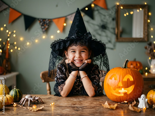 Happy little girl in witch costume with carved pumpkin for Halloween celebration