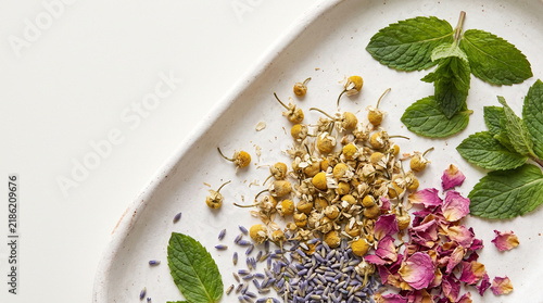 Herbal tea flat lay with chamomile, mint, lavender, and rose petals arranged on white ceramic tray for calming preparation