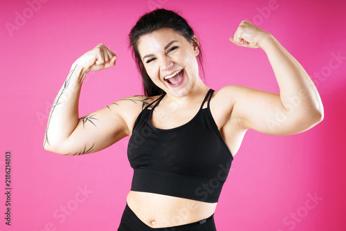 A cheerful athletic young woman shows off her muscular arms  the result of weight training at the gym  against a pink background