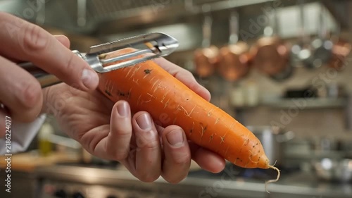 Professional chef's hands precisely peeling a fresh, organic orange carrot with a sharp hand peeler in a bright kitchen environment.
