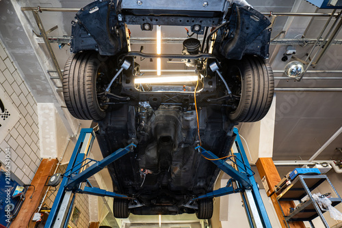 Wide angle undercarriage view of a car raised high on a hydraulic lift inside an auto repair shop.