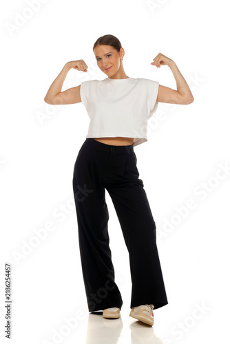 Full length fashion portrait of confident woman flexing arm muscles, strong pose, on white background.