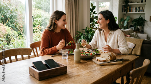 Two young women eating a healthy lunch together at a wooden dining table