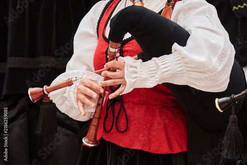 Close-up of a musician’s hands playing the chanter of a traditional Galician bagpipe, or gaita, while wearing a red and white regional folk costume.