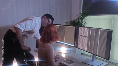 Programmers working at night analyzing code on monitors in a modern office. Software developers collaborating on debugging cybersecurity and data programming projects. Ai coding Software technician.