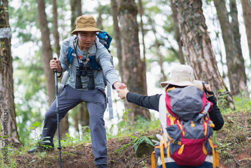 Male hiker reaches down to help his partner up a steep forest slope