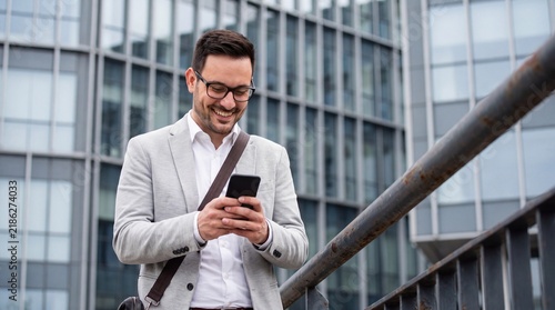 Smiling businessman using a smartphone while standing on a bridge near office building