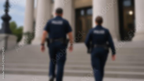 Blurred rear view of two police officers walking up stone steps to a courthouse