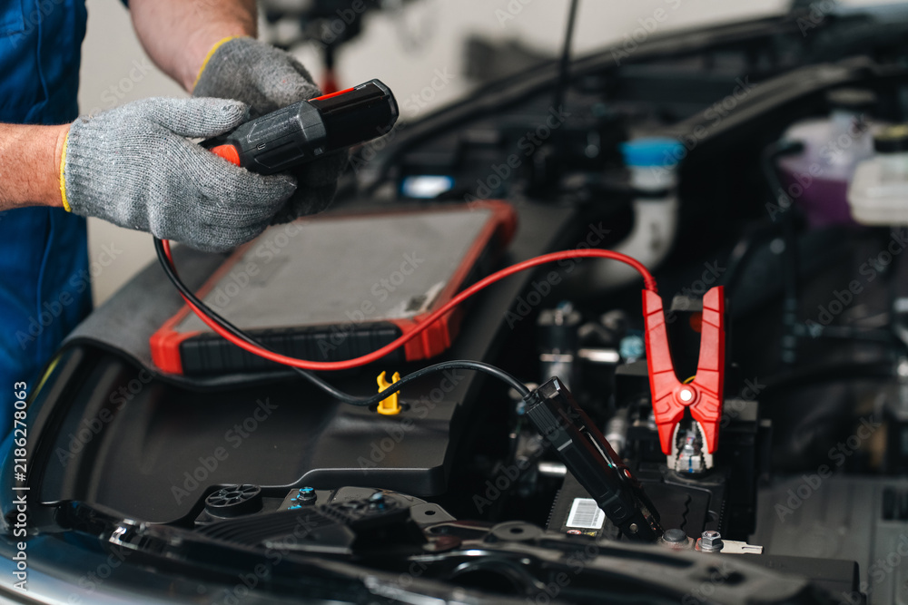 Obraz premium Electric vehicle car battery repair service Automotive mechanic testing car battery with red jumper cable and diagnostic tool