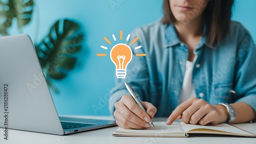 Woman writing in notebook with light bulb icon symbolizing a creative idea and business inspiration in office