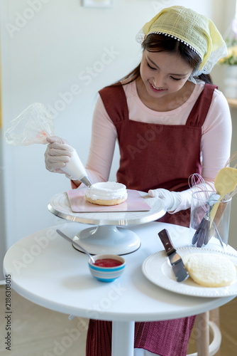 Young Girl Decorating Homemade Cake with Frosting Using Piping Bag in Bright Kitchen
