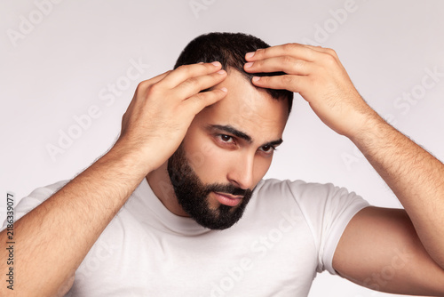 Bild auf Leinwand Guy examining receding hairline on forehead while touching scalp to check hair l