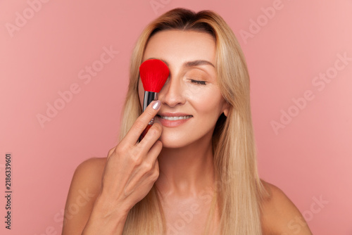 Cuadro en lienzo Playful woman covering eye with large red makeup brush smiling and enjoying dail