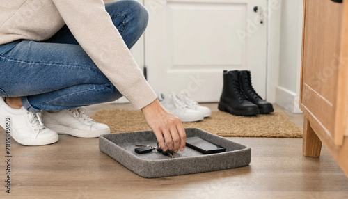 Person placing house keys in a felt tray on the entryway floor next to shoes with key tray home organization daily routine putting away keys entry hall modern interior returning home