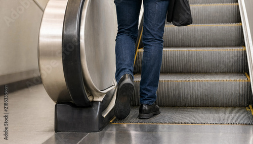 Legs of a person wearing jeans walking up an escalator in a public building with walking up public transport urban life moving staircase building interior moving stairs urban commute