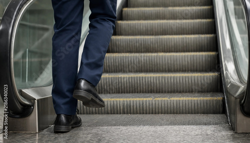 Person in dark trousers standing on the steps of an escalator moving upwards with moving stairs public transport escalator trousers commuting infrastructure movement standing footwear