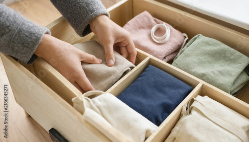 Woman hands organizing folded clothes and fabric pouches inside a wooden drawer organizer with folding clothes closet organization organized drawer tidy home minimalist storage tidying