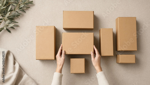 Top view of person hands arranging various cardboard shipping boxes on neutral background with e commerce delivery service online shopping small business supply chain parcel delivery