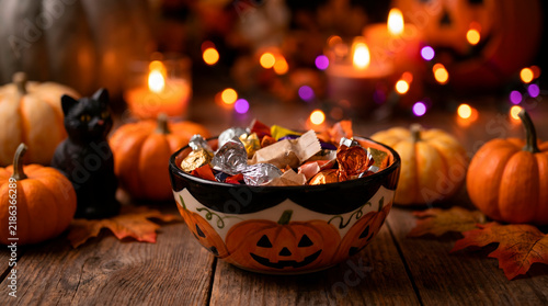 Ceramic Halloween candy bowl filled with assorted treats on a rustic wooden table with pumpkins