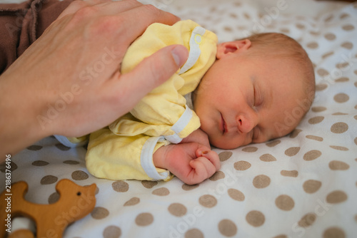 Parent hand gently resting on a newborn baby sleeping soundly in a crib, symbolizing protection, care, and the beginning of new life with parental love