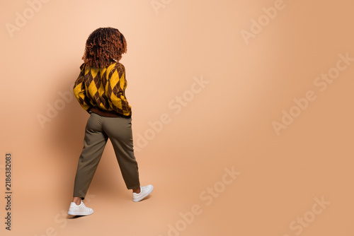 фотографія Woman in argyle sweater walking away on neutral background, casual fashion portr