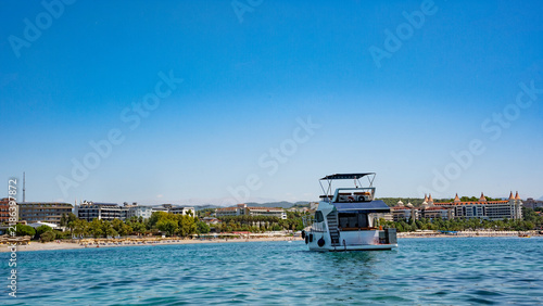 A white yacht sailing on clear blue waters near a sandy beach, surrounded by a vibrant shoreline on a sunny day.