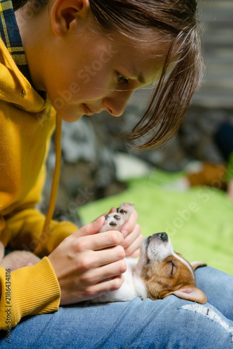 Preteen holding a new puppy face with joyful happy excitement outdoors on the grass. Pet owner adopting and caressing small dog with tender loving care in natural light near a garden.