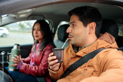 Young Hispanic man drinking yerba mate while sitting in car with female friend during road trip