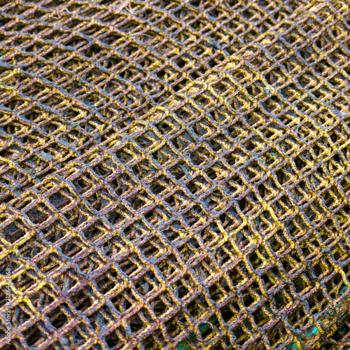 A detailed close-up of piled, textured yellowish-brown commercial fishing nets on a deck, featuring complex mesh patterns, knots, and a visible yellow hardware ring.