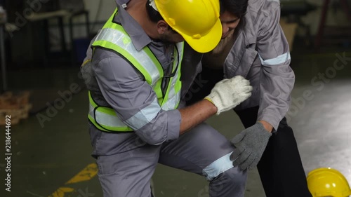 Industrial worker assists injured worker with safety helmet and reflective vest after workplace accident, emergency response, colleague concern and teamwork during workshop safety training