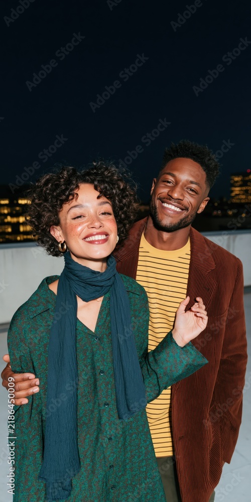 Obraz premium Smiling couple on a rooftop at night portrait with city skyline and scarves for lifestyle banner and background design use