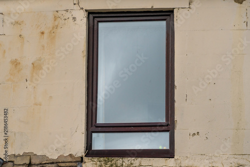 Obraz na płótnie Rectangular, dark brown framed  window centered on a light pinkish-beige, weathered exterior wall
