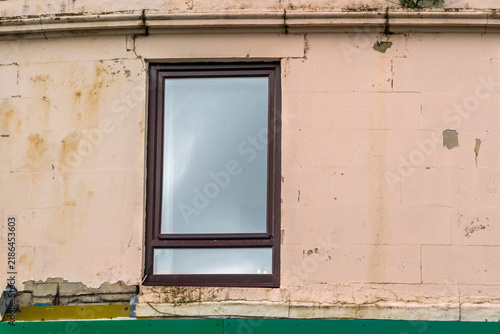 Fotografie Rectangular, dark brown framed  window centered on a light pinkish-beige, weathered exterior wall