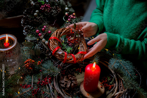 Hands crafting a rustic Christmas wreath with pine, berries, and candles