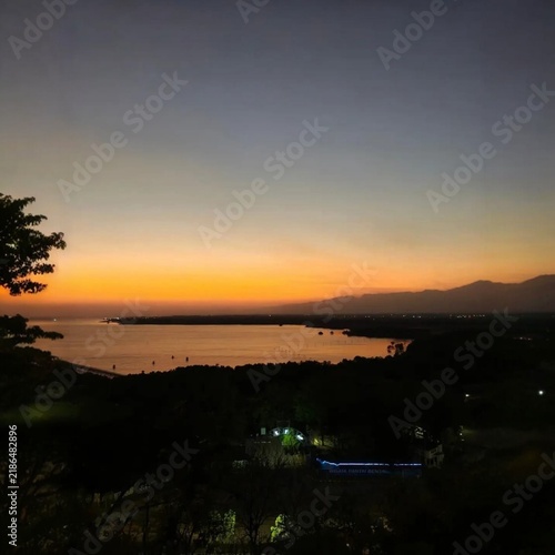 Bild auf Leinwand Vertical shot of beautiful twilight view over a tranquil coastal bay with silhouetted mountains and far-off town lights