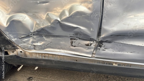 Close up of a severely dented silver car door with deep scratches, damaged metal and visible impact marks