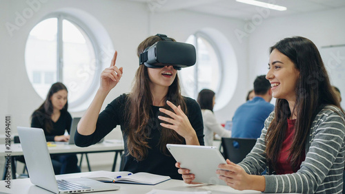 Young woman wearing a virtual reality headset interacting with digital interface in a modern office with colleagues