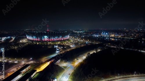 A mesmerizing night shot of Warsaw with PGE Narodowy, Świętokrzyski Bridge, and the city's dazzling lights.