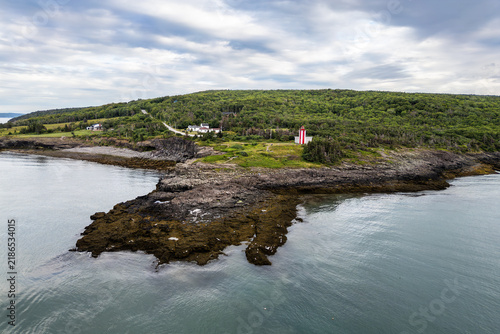 фотографія Red-and-white lighthouse on a rocky headland along the wooded coast of Brier Island beneath a vast, cloudy sky