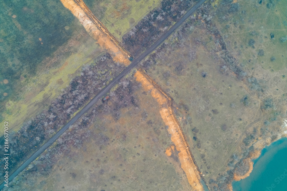 Obraz premium Earthworks and anti tank ditch line constructed along reservoir shoreline, high angle top view aerial drone shot
