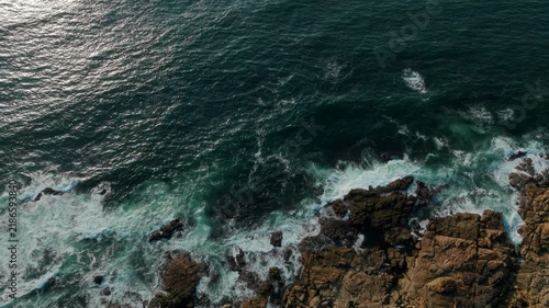 Mesmerizing top-down aerial view of turquoise Atlantic waves crashing against rugged, sun-drenched coastal rocks near A Guarda, evoking a powerful sense of raw natural energy, coastal serenity, and