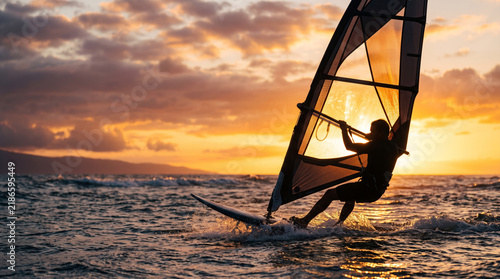 Obraz na płótnie Windsurfer riding waves at sunset with dramatic clouds and ocean spray