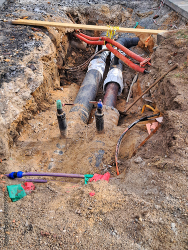 Excavated trench in dirt showing exposed underground utility pipes and cables undergoing repair work on a street in Prague.